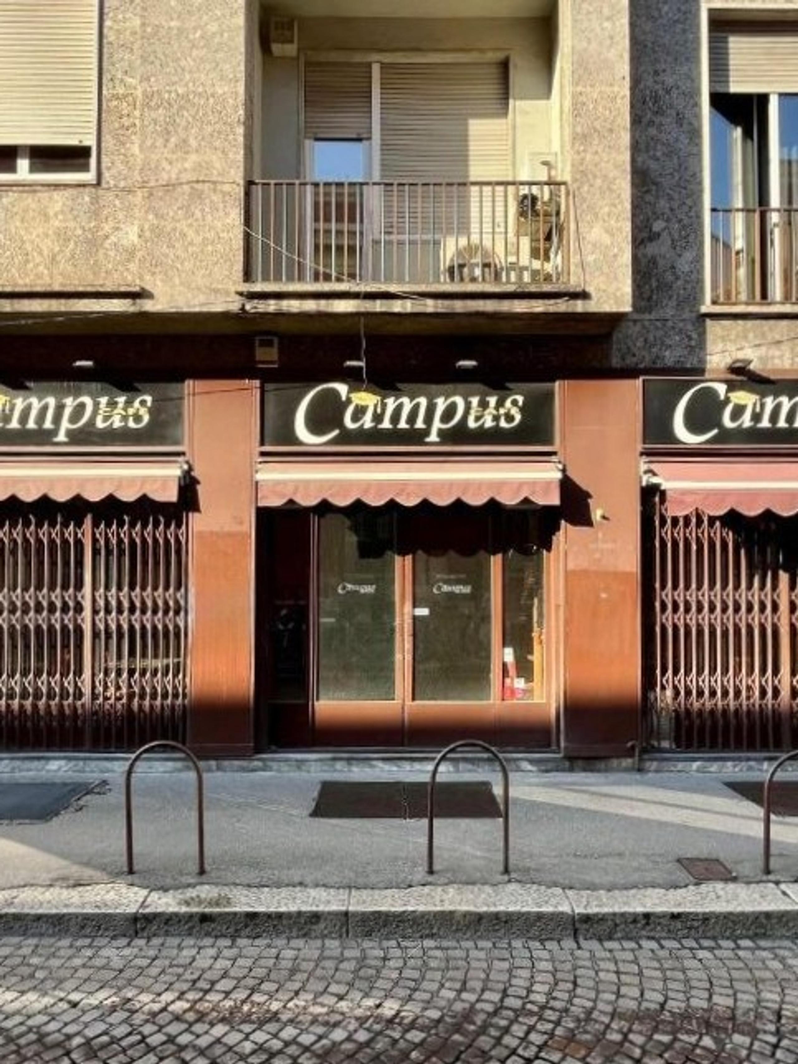 facciata di un bar di fronte alla statale di Milano, saracinesche chiuVetrine chiuse, locale chiuso, marciapiede, pavè, edifici con finestre e balconi