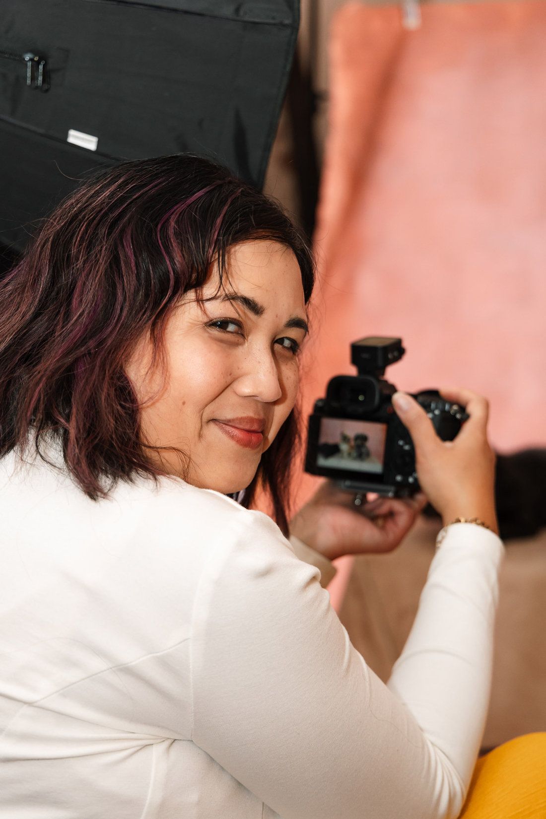 Pet photographer Ina J in the studio looking back over her shoulder, her camera showing a photo on its screen
