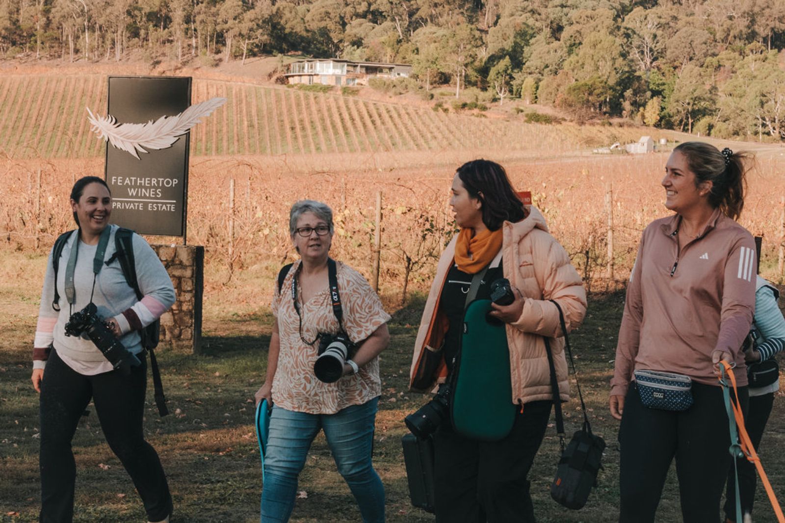 Four photographers carrying cameras walking past a Feathertop Wines vineyard sign on a workshop