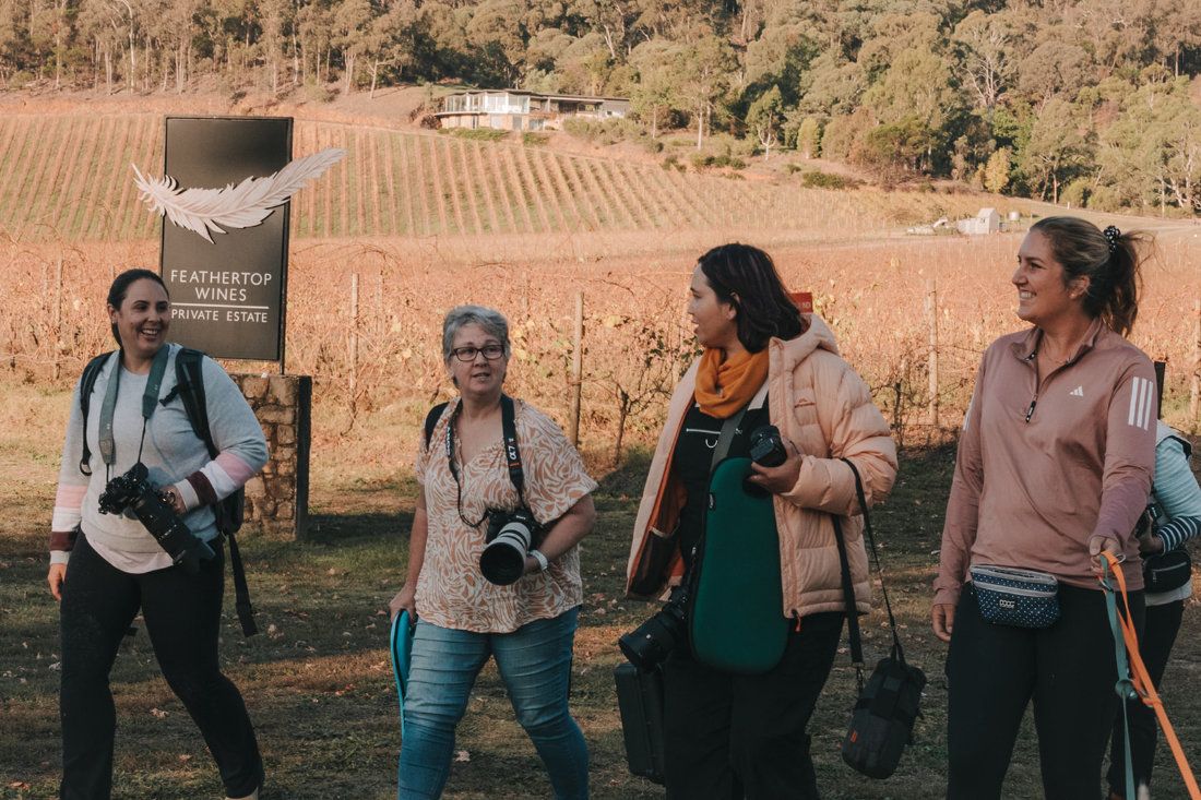Four photographers carrying cameras walking past a Feathertop Wines vineyard sign on a workshop