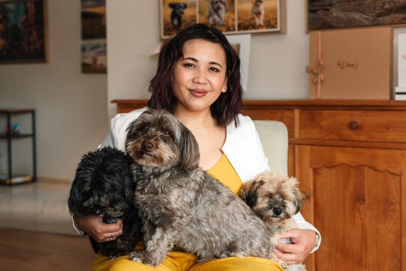 Pet photographer Ina J in a white cardigan seated with three small dogs on her lap in her studio