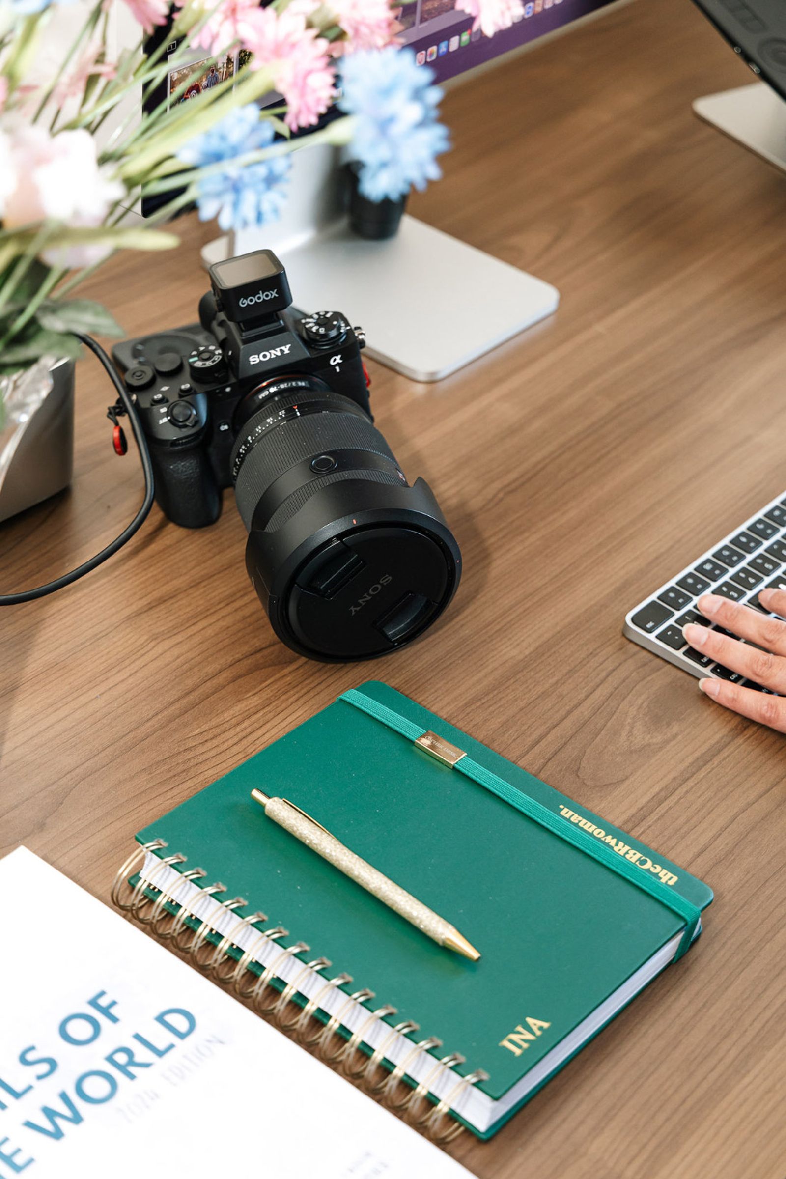 A desk flatlay with a Sony camera, a personalised notebook and a Tails of the World book
