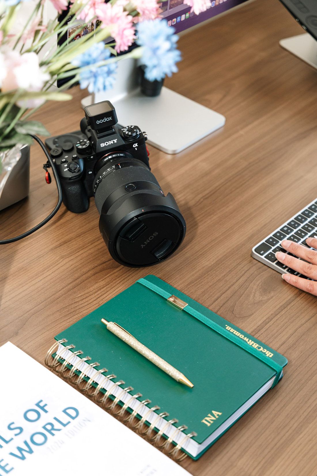 A desk flatlay with a Sony camera, a personalised notebook and a Tails of the World book