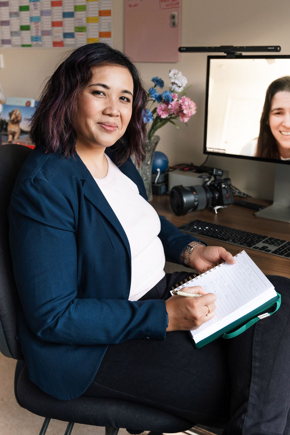 Pet photographer Ina J in a navy blazer taking notes at her desk during a video coaching call