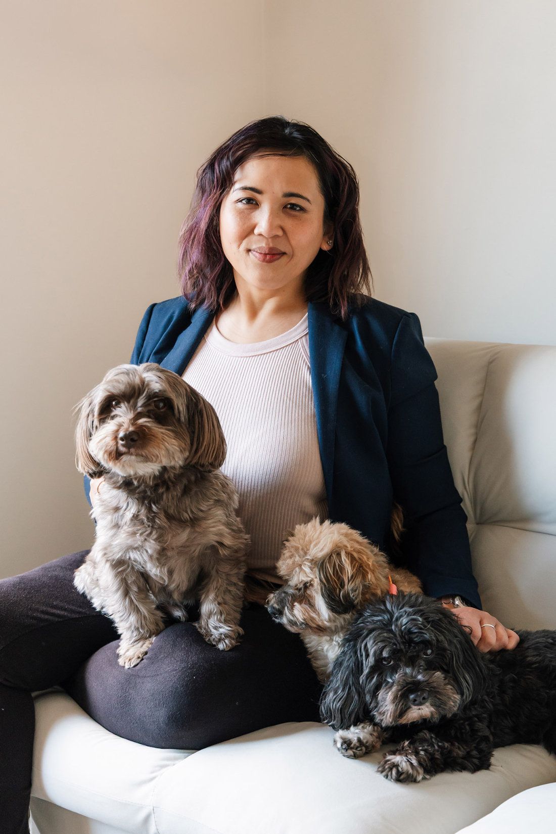 Pet photographer Ina J in a navy blazer sitting on a white sofa with two small dogs
