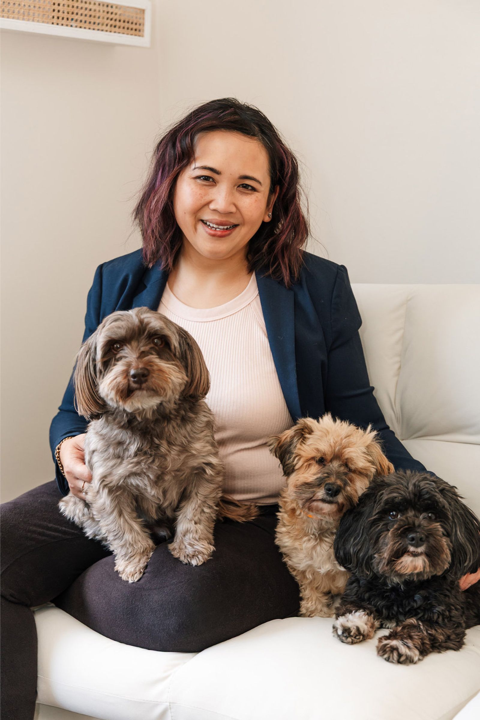 Pet photographer Ina J in a navy blazer on a white sofa with three small dogs
