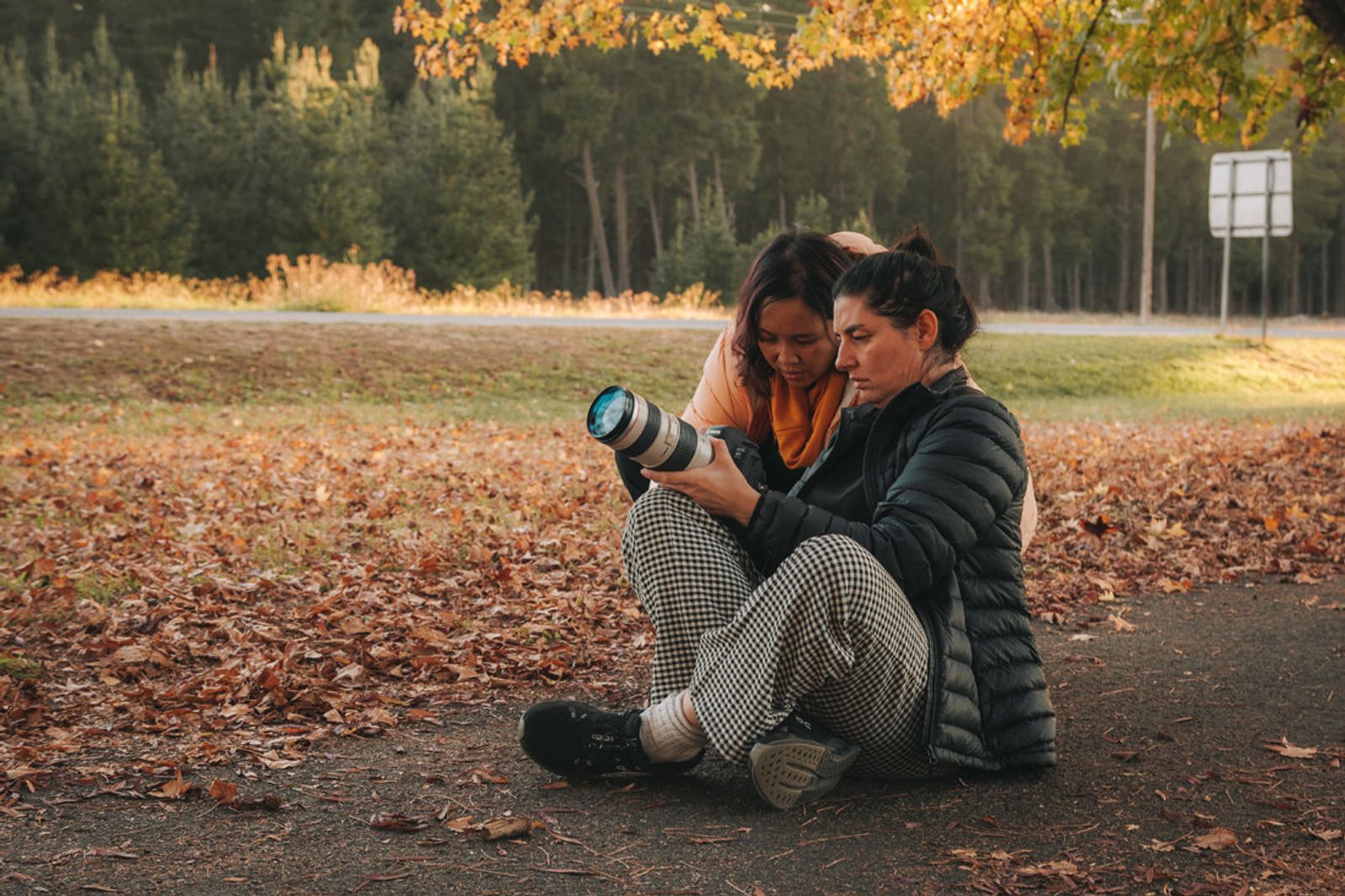 Two photographers sitting on the ground reviewing a photo on a telephoto camera together at sunset