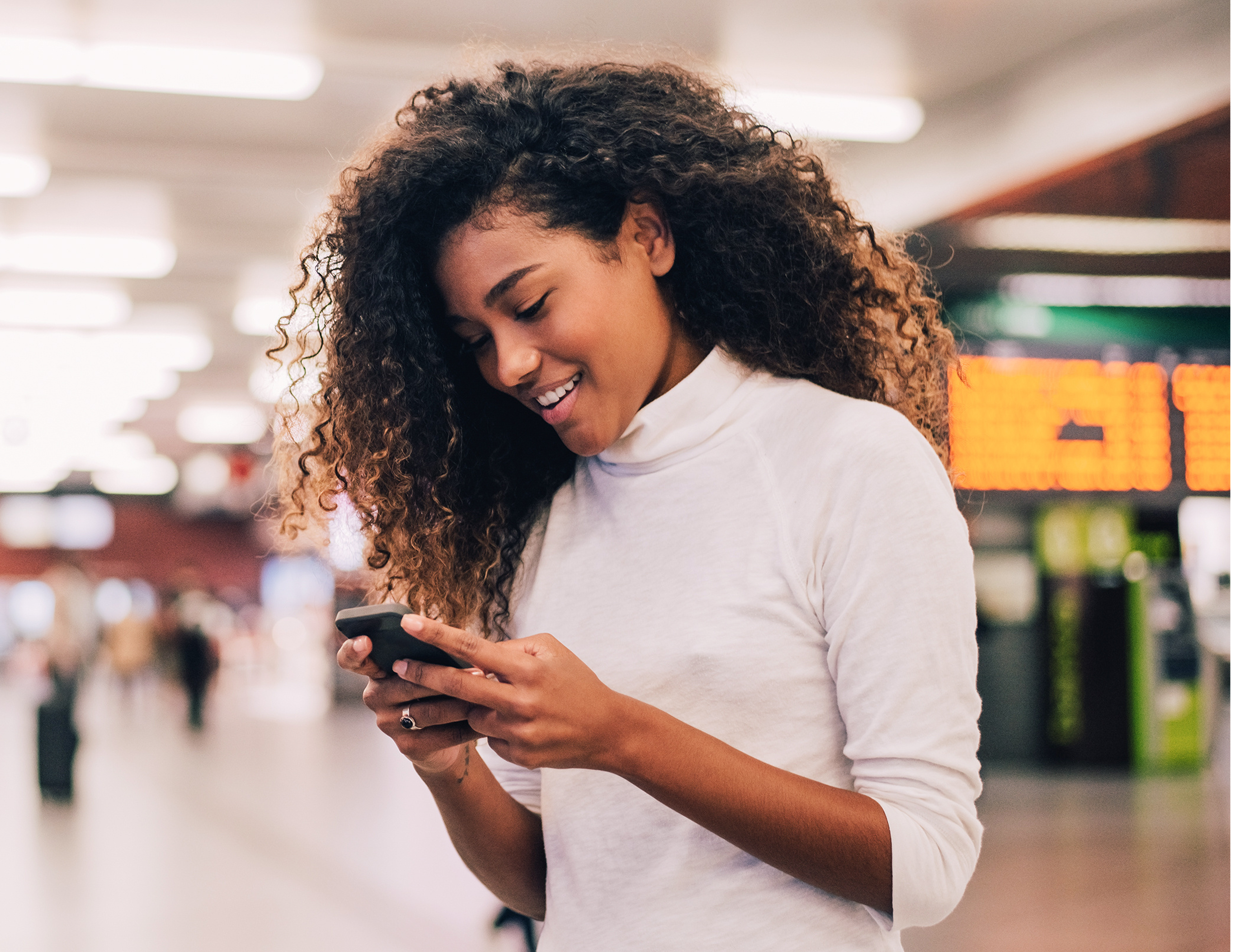 Young woman in a train station smiling and looking at her phone