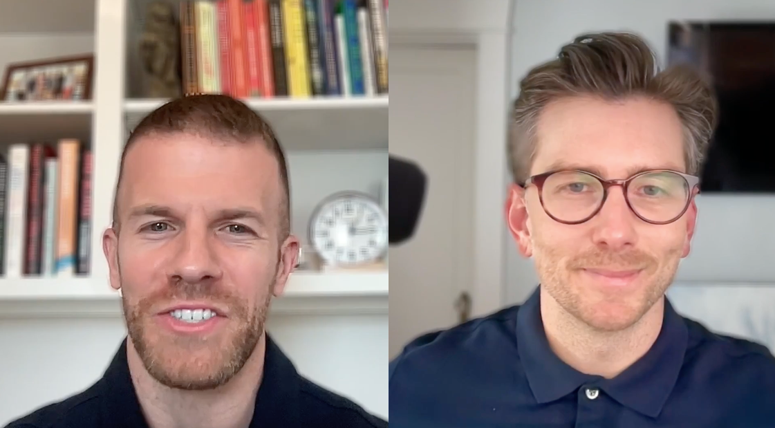 Two men smiling during a video call, with one in front of a bookshelf and clock, while the other is against a white wall and wearing glasses.