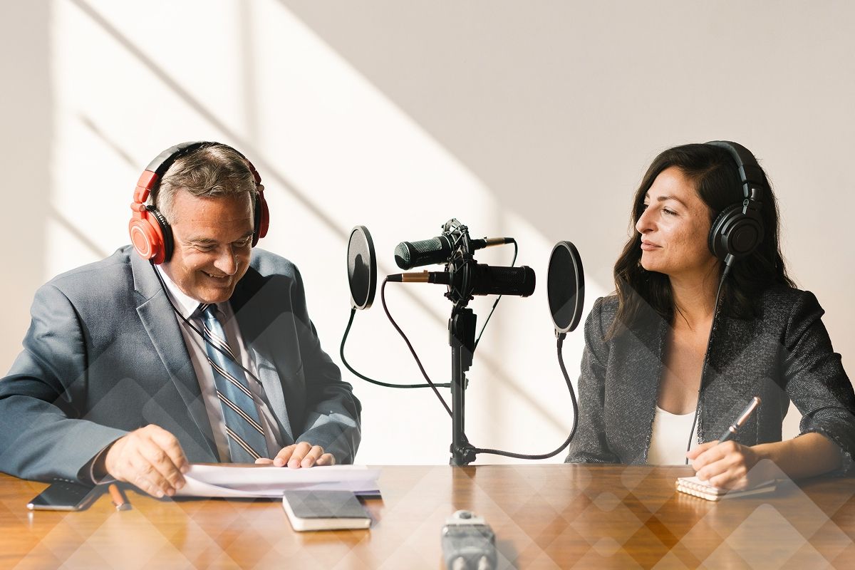 A man and a woman wearing headphones record a podcast with a microphone.