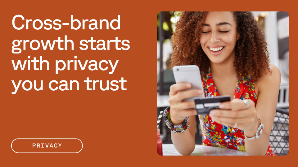 A woman with curly hair, wearing a floral top, smiles while holding a smartphone and a credit card. The text beside her reads, "Cross-brand growth starts with privacy you can trust."
