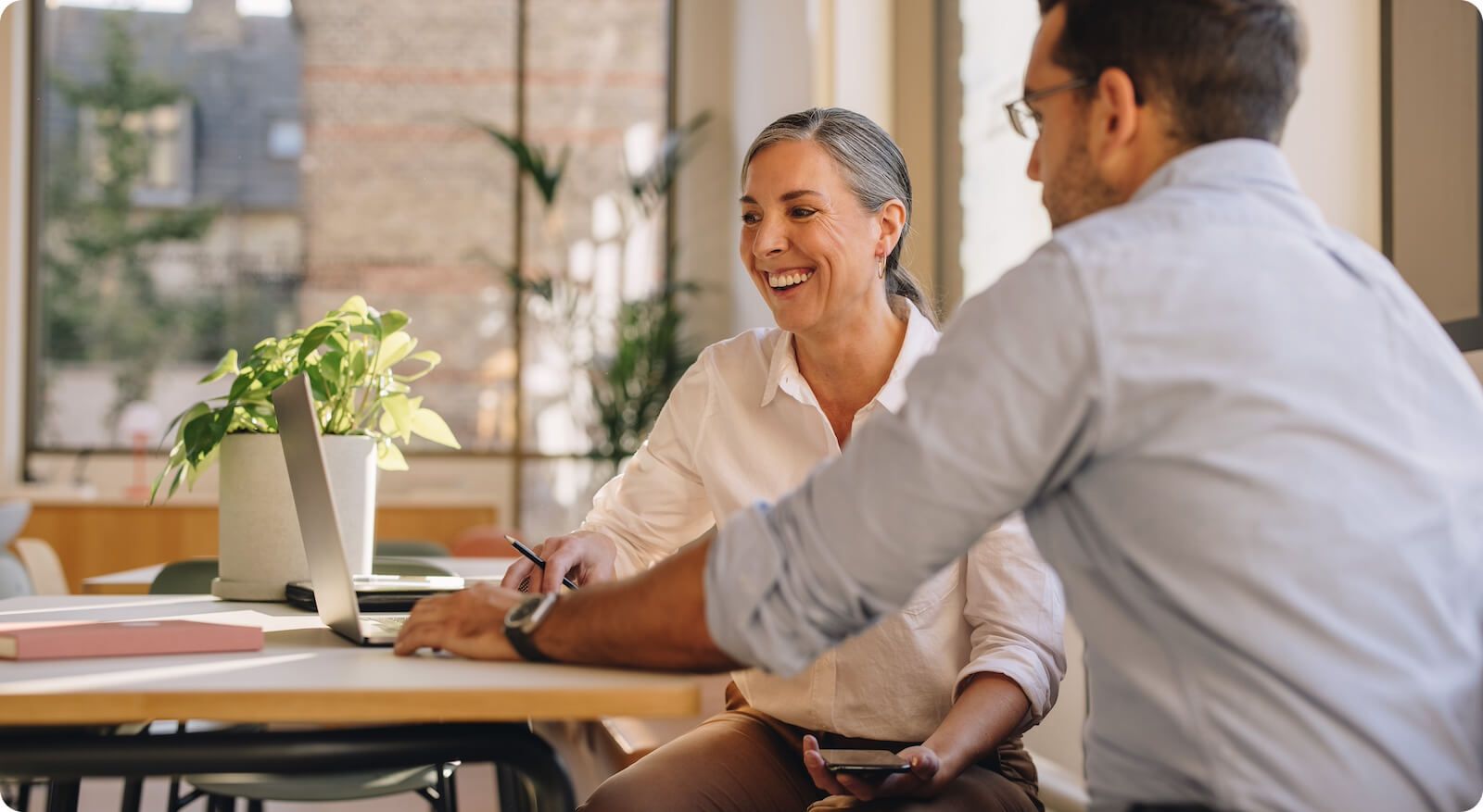 An older woman and younger man working in an office and laughing at desk
