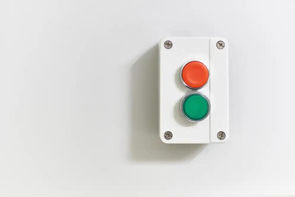 A white panel features two circular buttons, one red on top and one green below, mounted on a white wall.