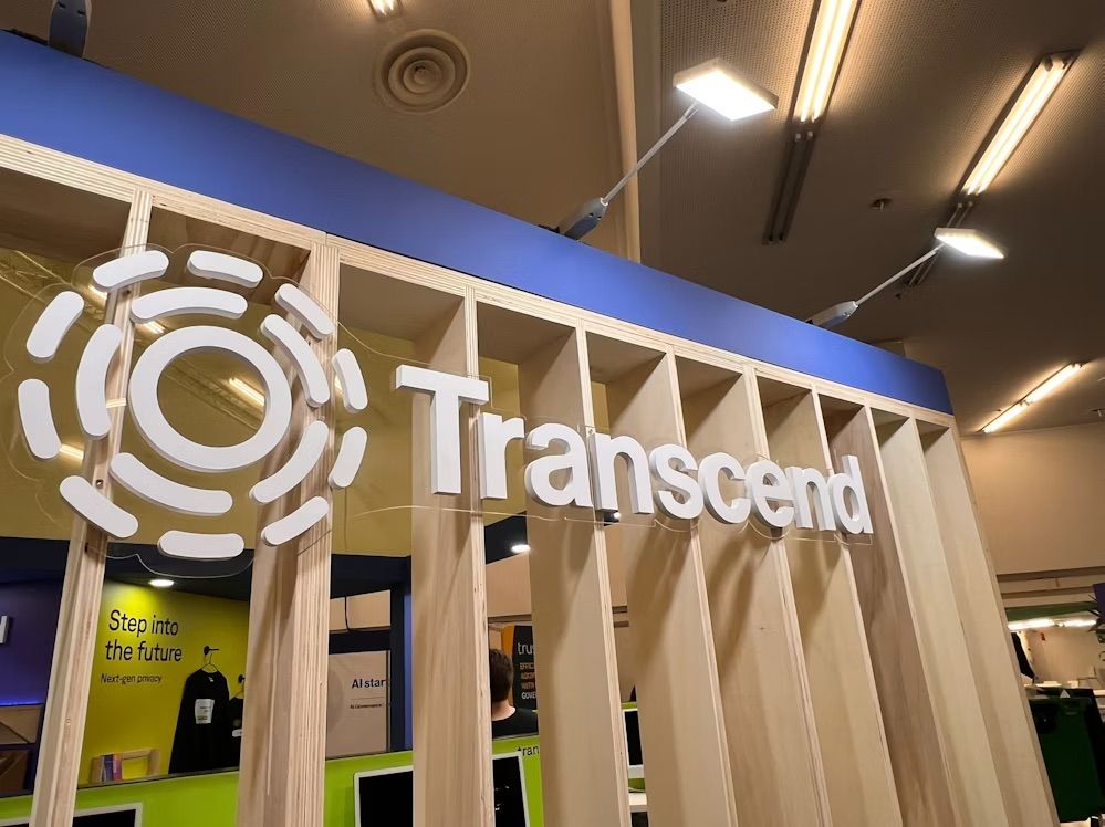 Large white transcend logo in front of trade show display booth with wooden pillars