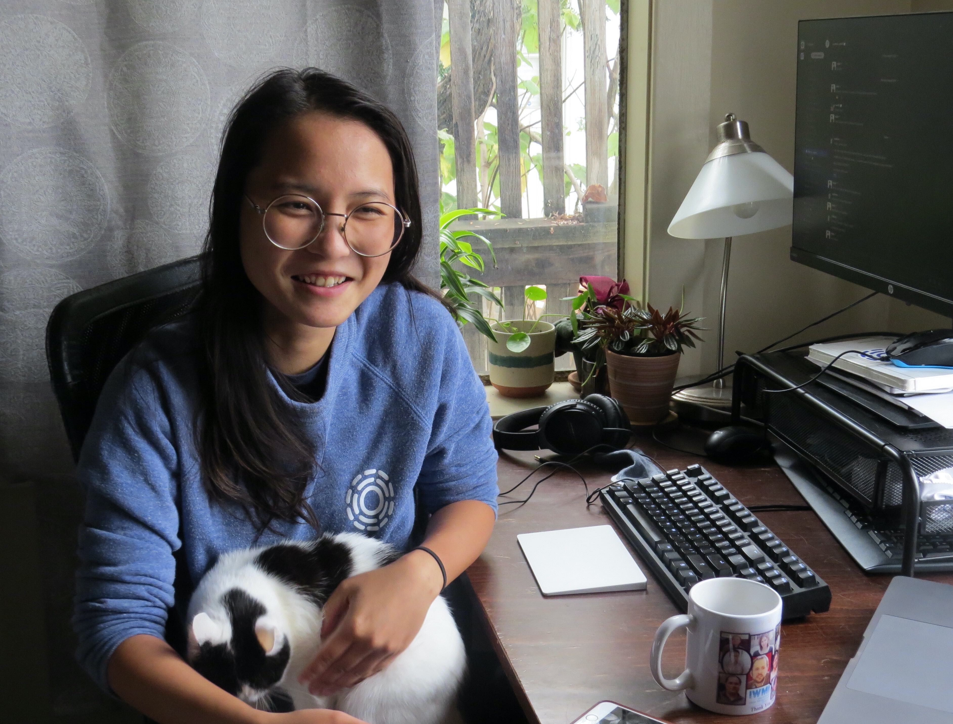 Minh Nguyen at her desk with a white and black cat in her lap