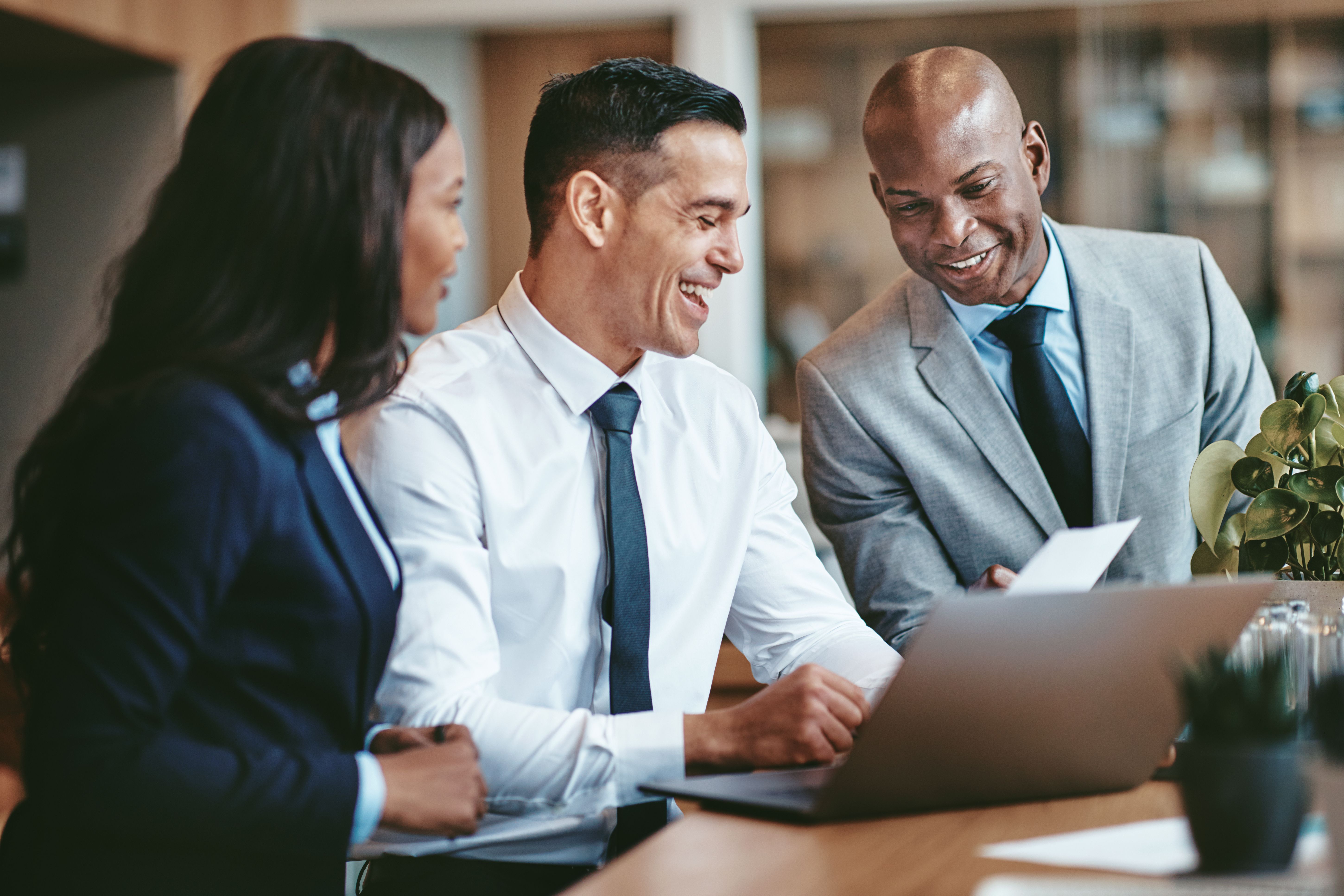 Three executives smiling and looking at a laptop