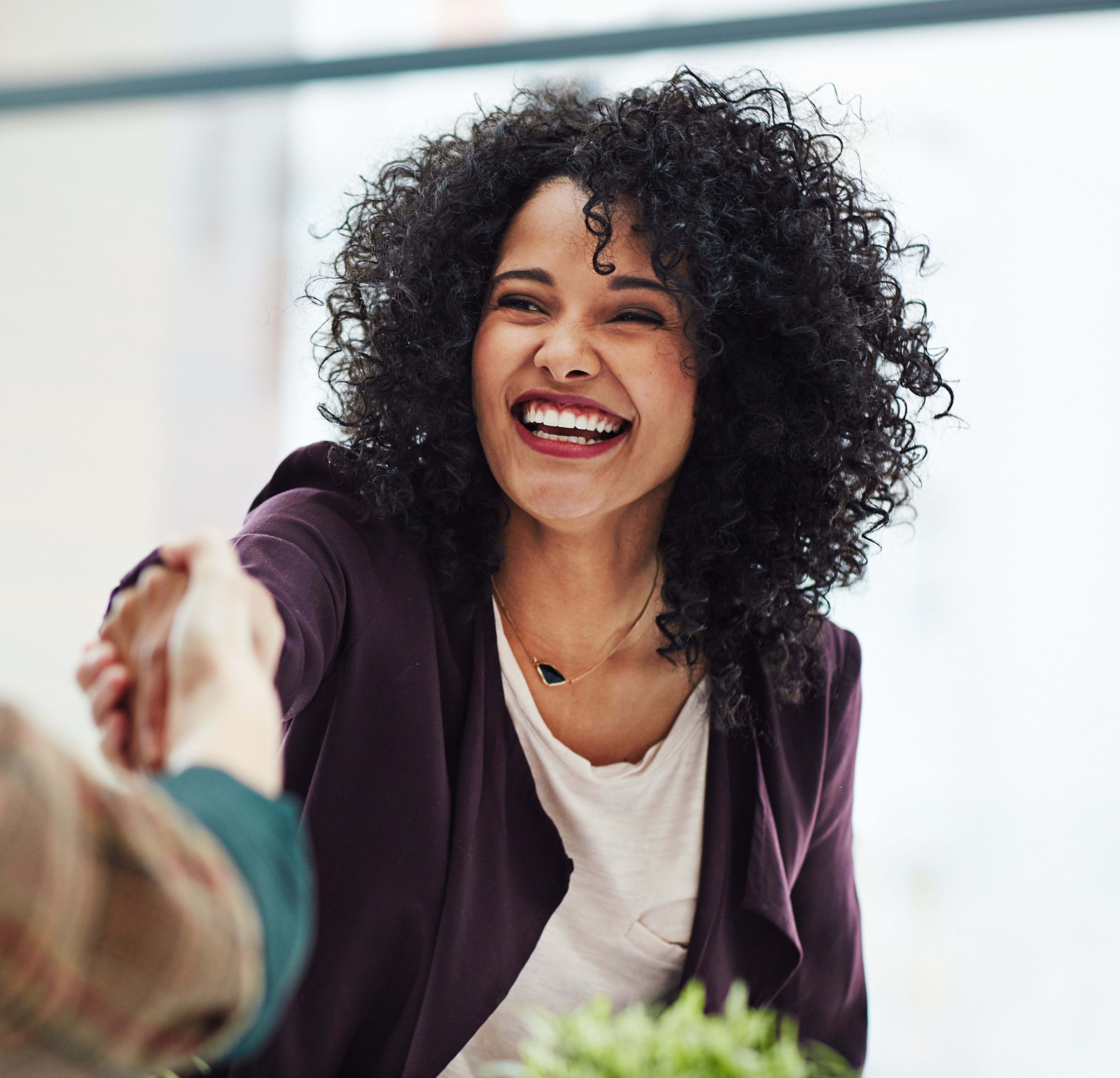 A photo of a woman smiling while shaking hands with someone out of shot.