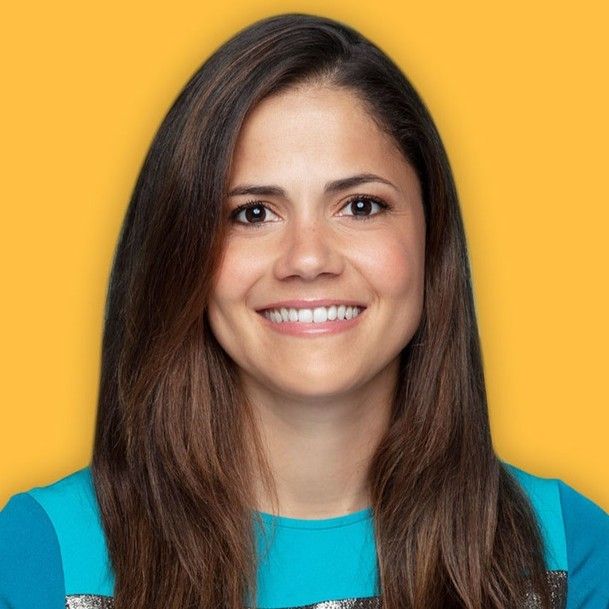 A person with long brown hair smiles while wearing a blue top, set against a bright yellow background.