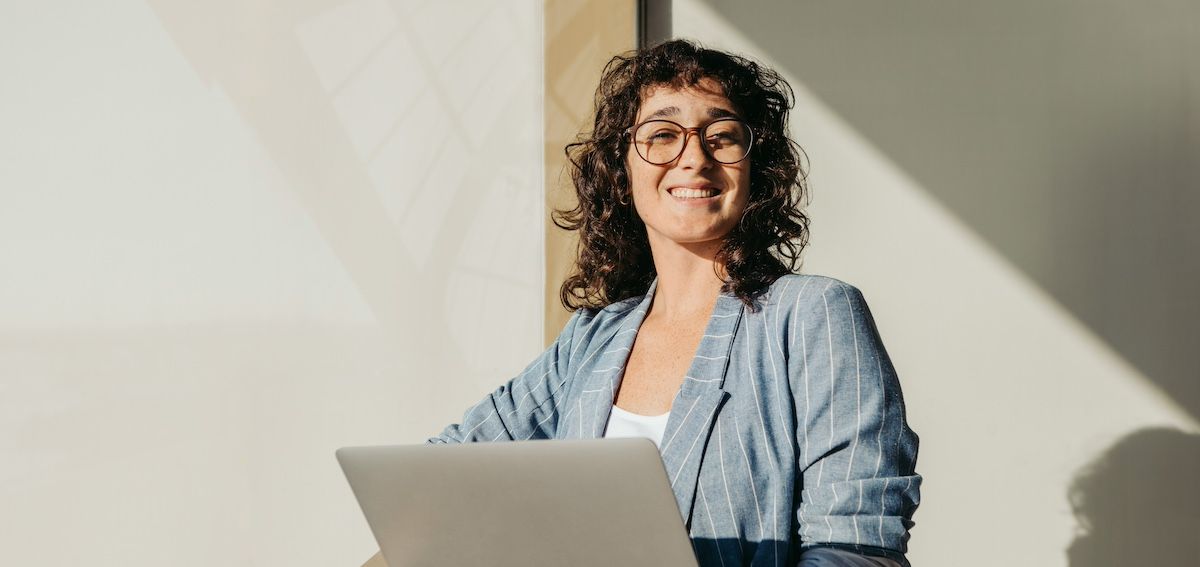 Professional woman with a laptop smiling as the sun hits her face in an office