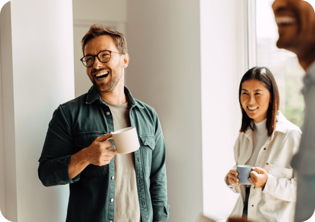 Photograph of man laughing over coffee with coworkers in a professional setting.