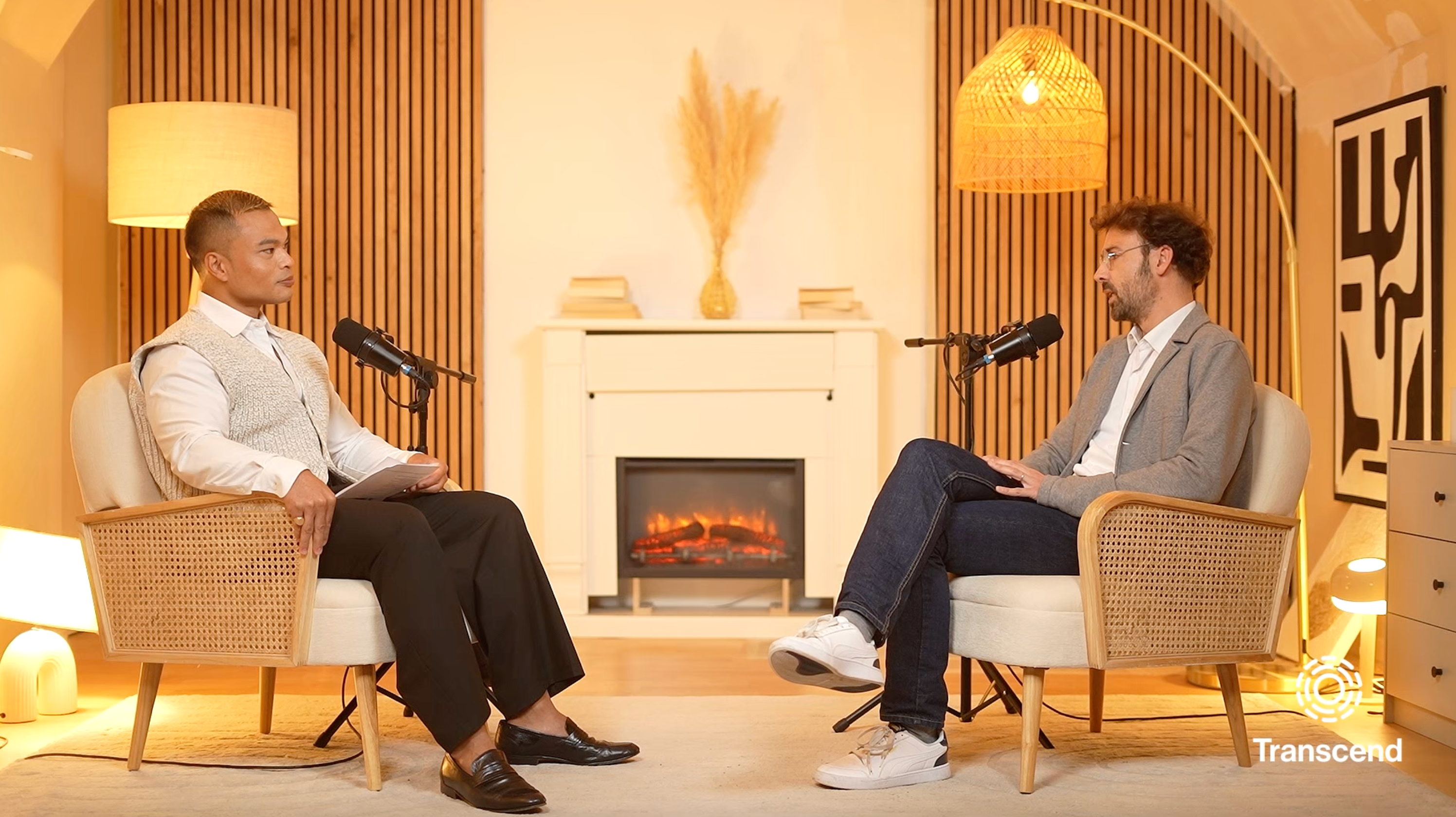 Ron De Jesus and Felicien Vallet sitting by a fire with microphones while recording a podcast