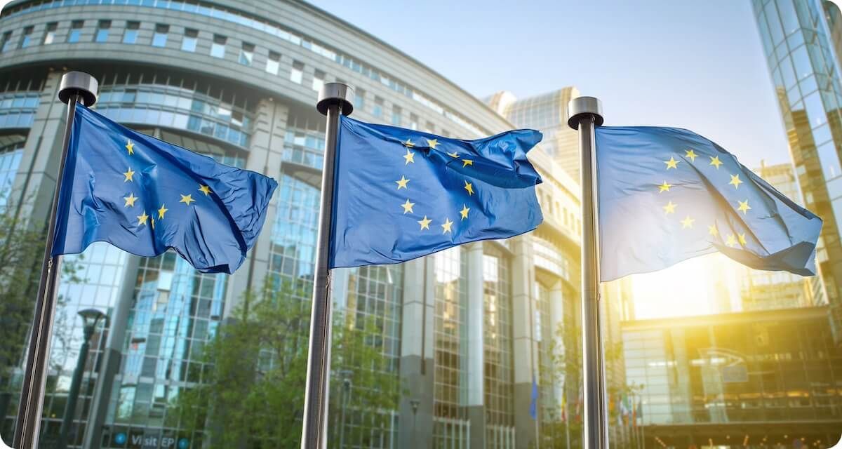 Three EU Flags flying in front of an urban city setting