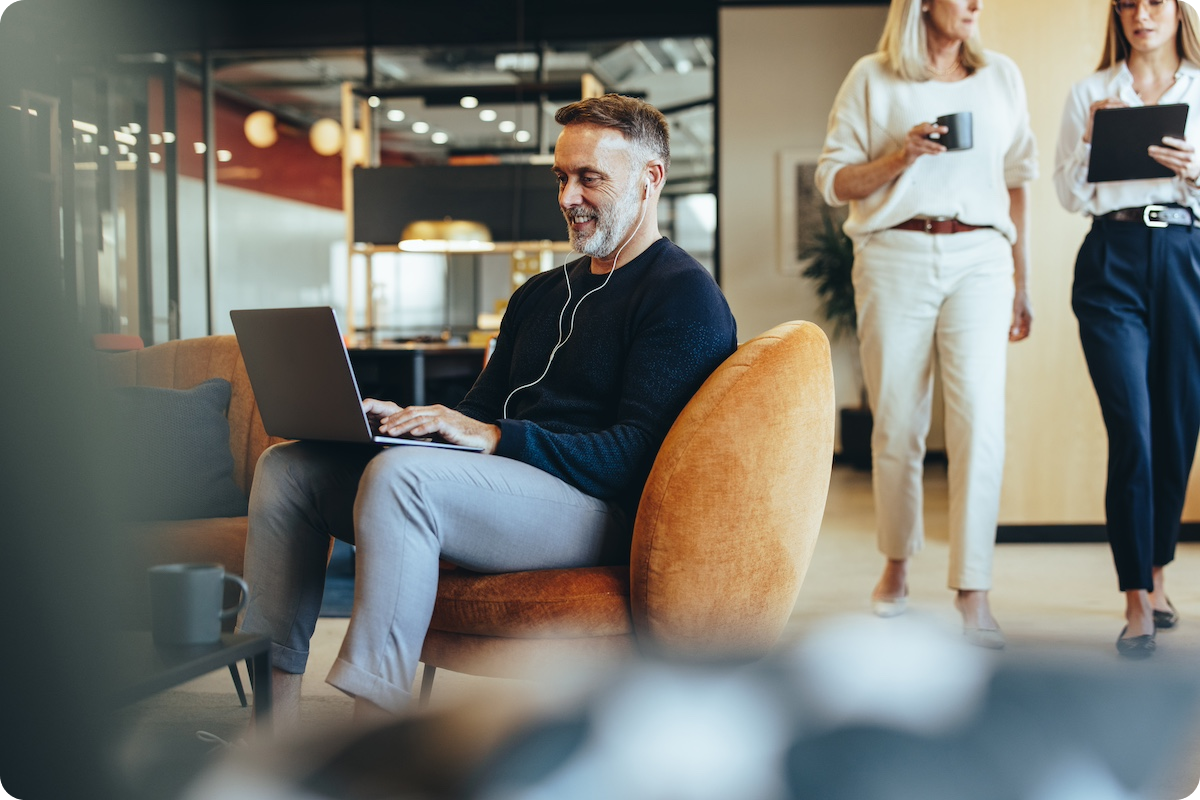 Experienced business man sitting in a modern office using a laptop and earbuds