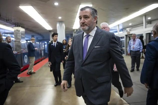 A man in a suit and tie walks through a train station platform, accompanied by several other people. The setting appears to be a busy, indoor public transport area with a train in the background.