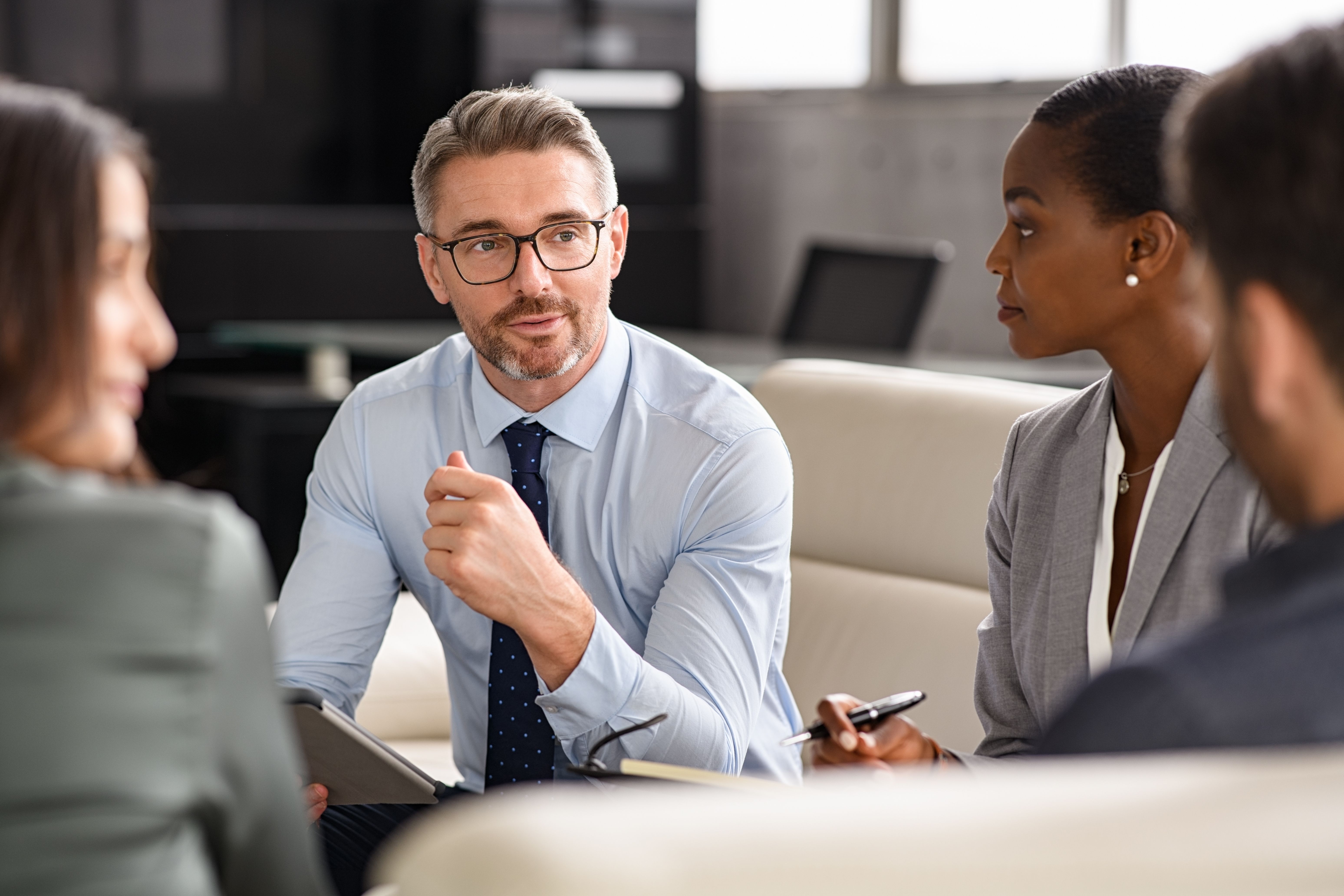 A man in a tie speaking in a business meeting, with two women listening.
