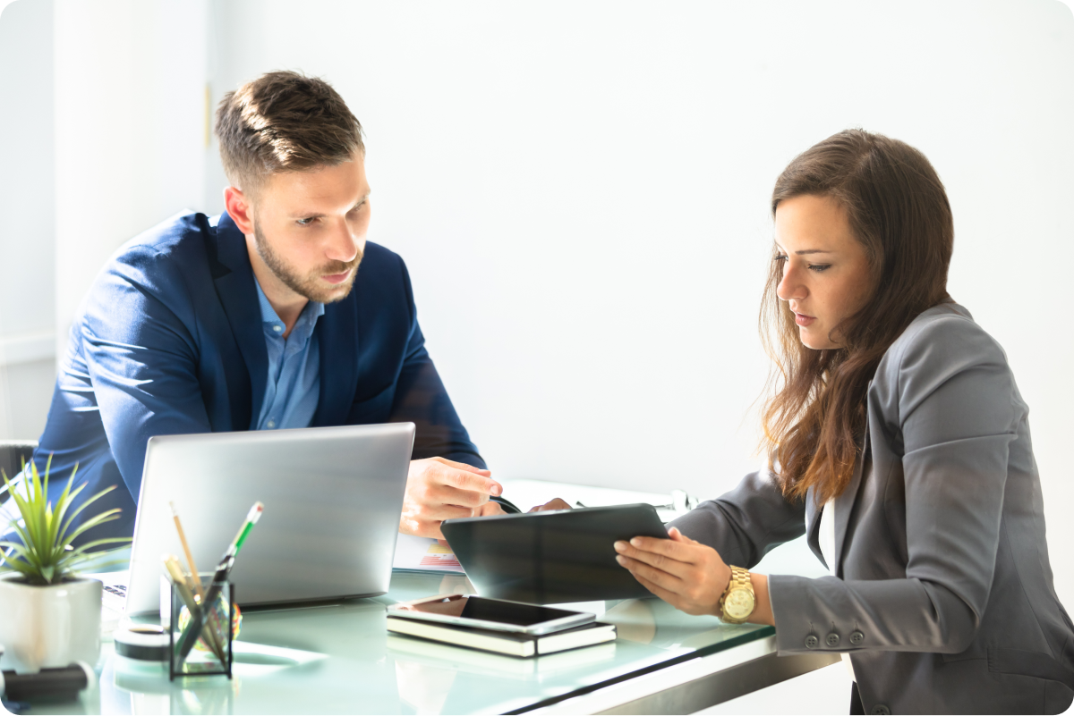 A professional man and woman reviewing a tablet at an office desk