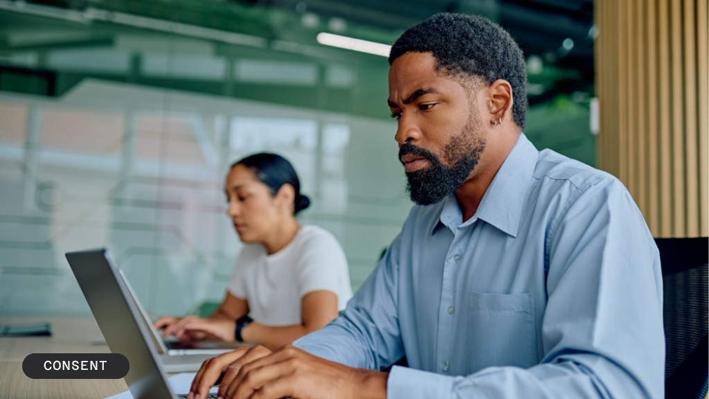 A man and a woman work on laptops in an office, with a "BLOG / CONSENT" banner.