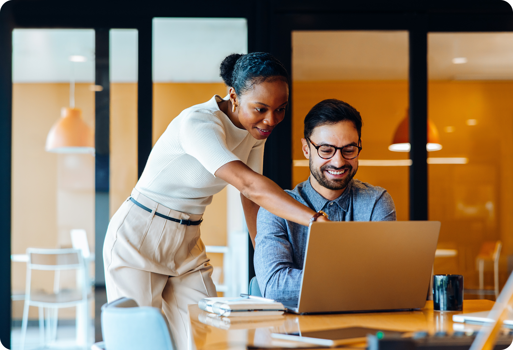 Two smiling colleagues collaborating on a laptop in an office.