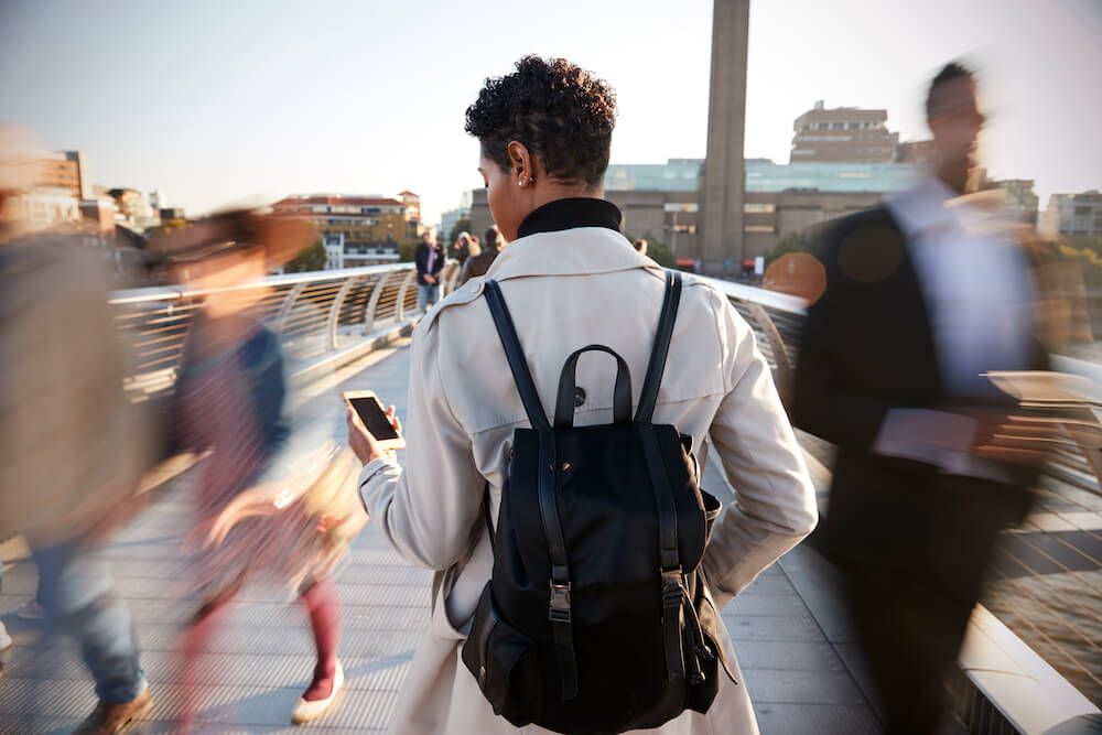 Traveler crossing bridge using their phone while people blur past them