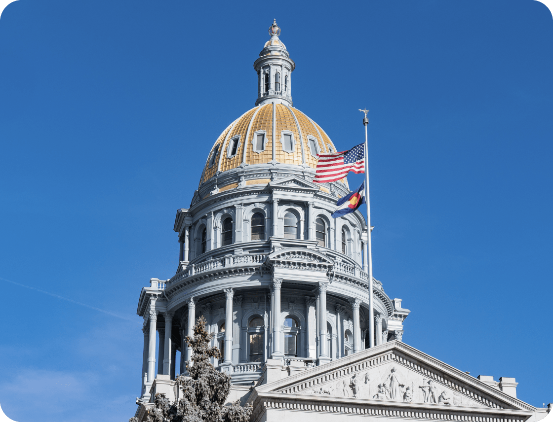 Colorado state capitol building with US and CO flags waving in front of blue sky