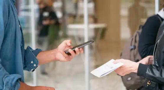 Close-up of one person holding smartphone and another holding piece of paper