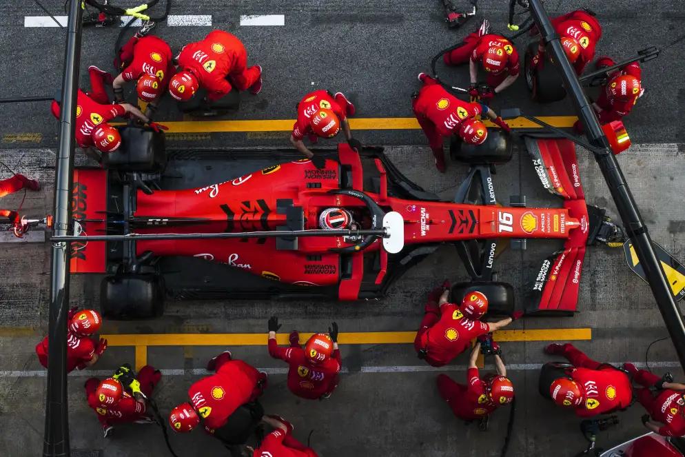 A Formula 1 race car in the pit stop is surrounded by a team of mechanics in red uniforms who are attending to various tasks on the vehicle.