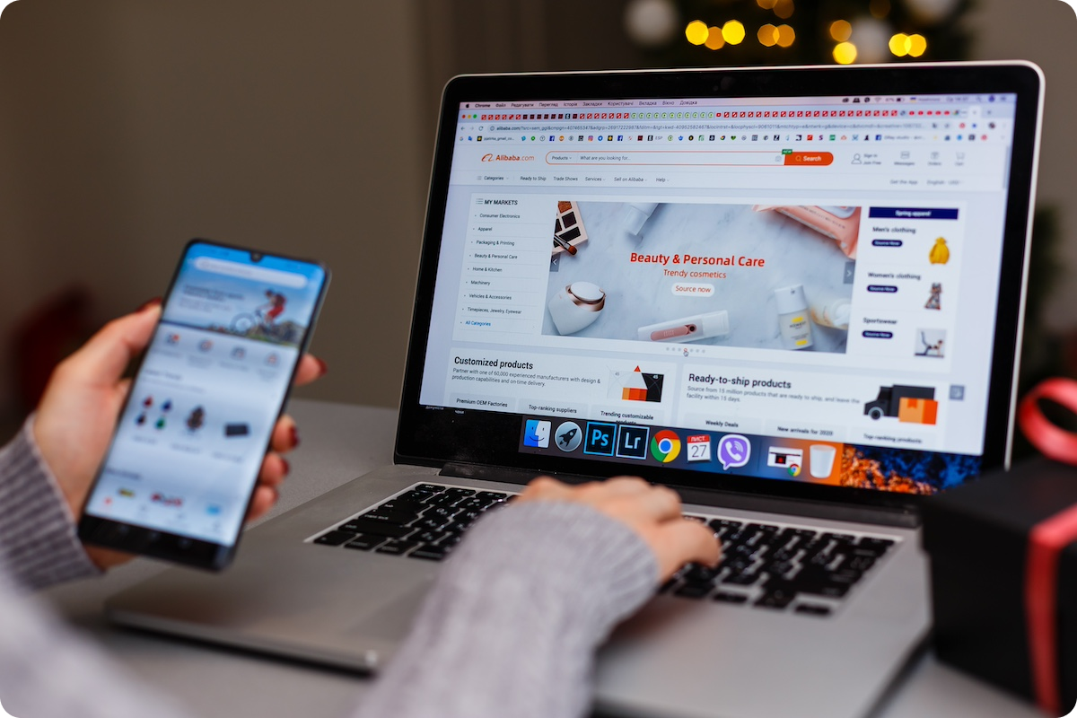 View of hands holding phone and using laptop to browse alibaba