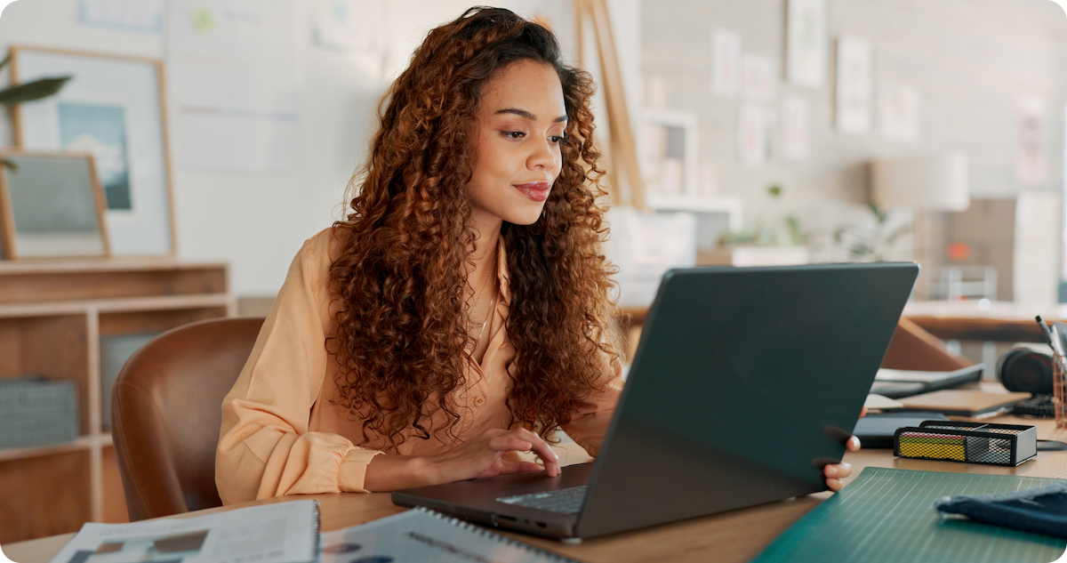 Woman with long curly brown hair using laptop in creative studio office space