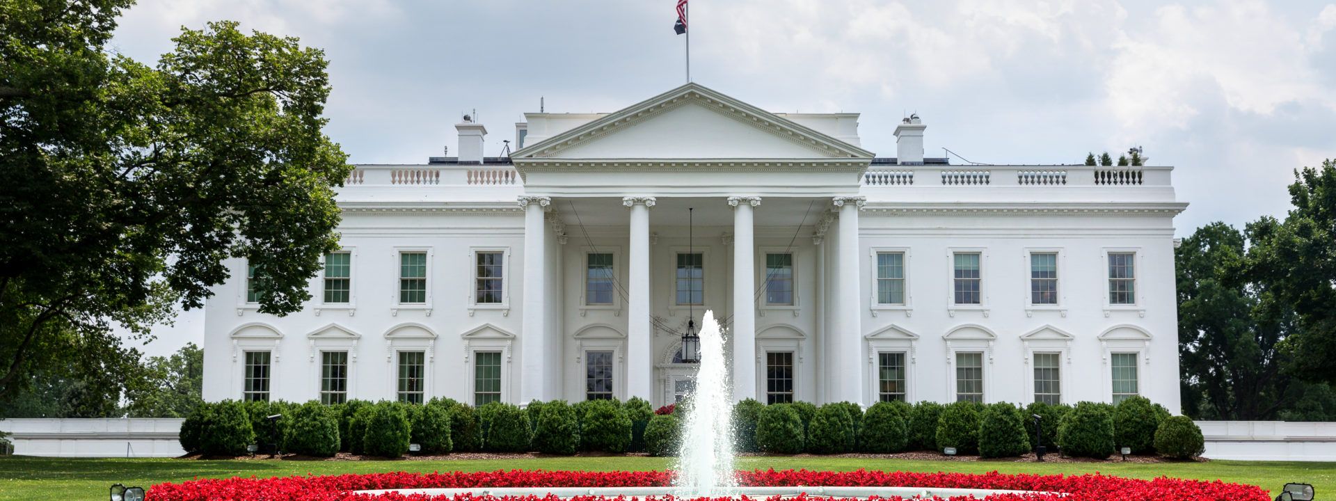 Facade of white house showing fountain bushes and American flag
