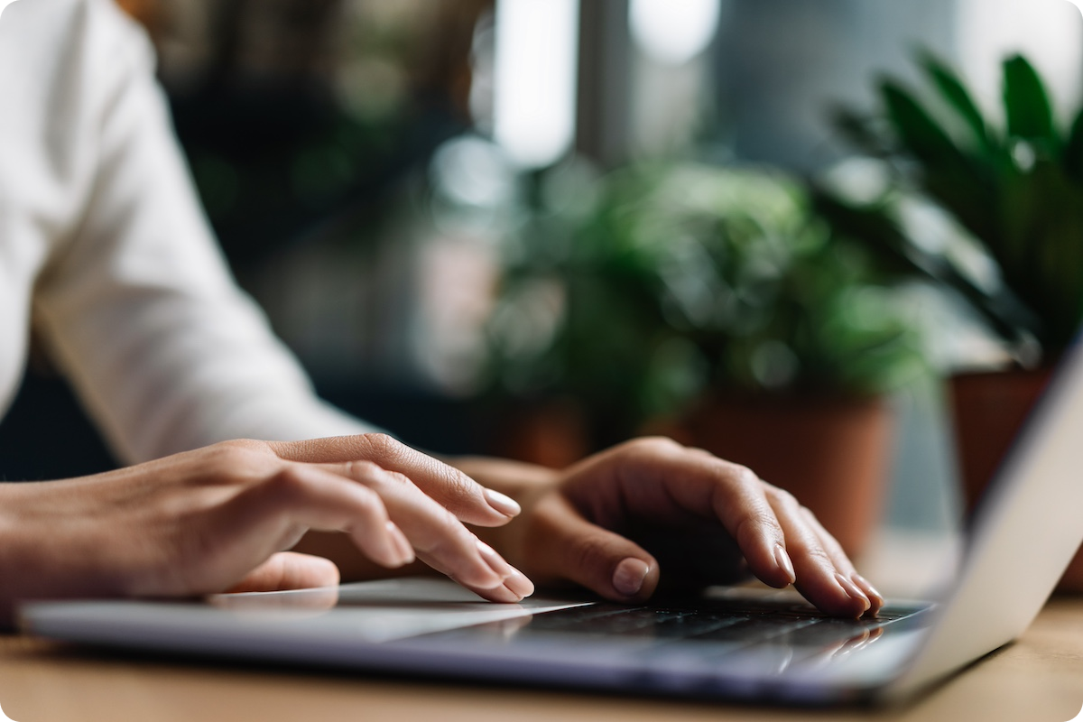 Close up of hands using laptop in front of blurred plants