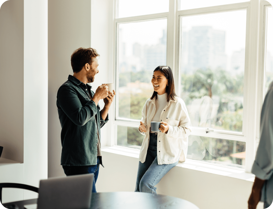 Two smiling professionals drinking coffee in a well-lit office