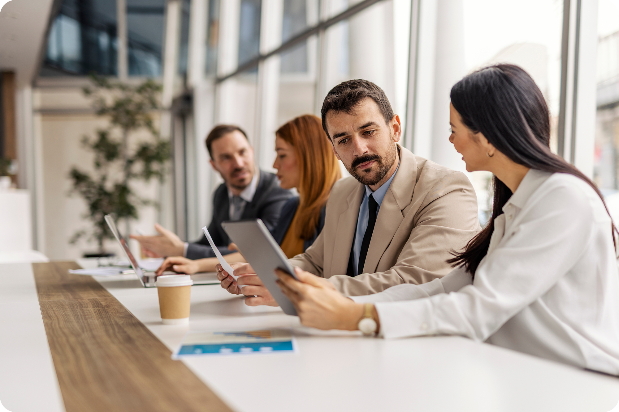 Executives at a large conference table looking a tablet