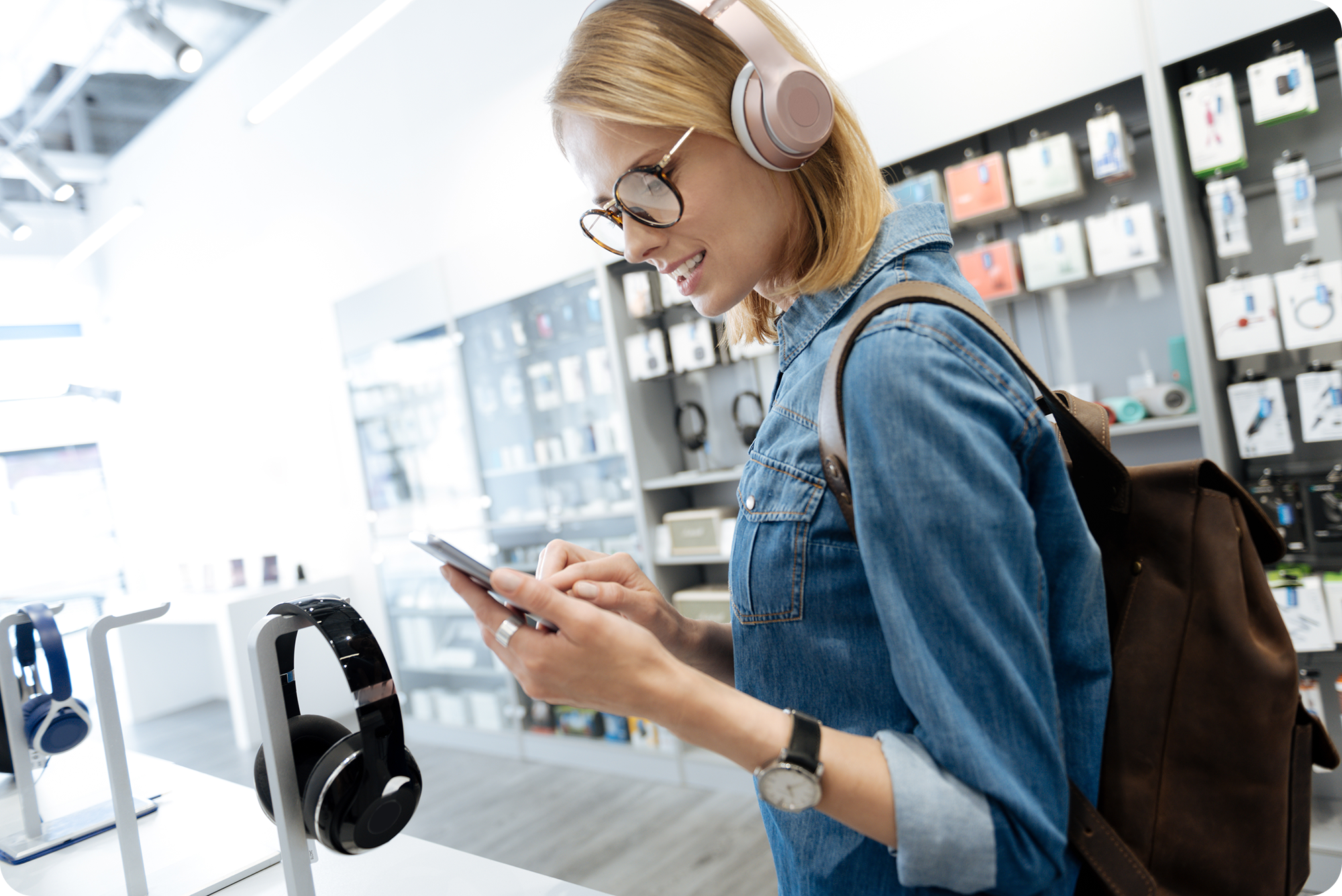 Young woman wearing over-the-ear headphones while looking at her phone in an electronics store