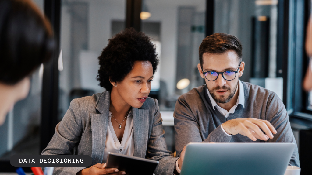 A man and a woman collaborate while looking at a laptop, one holding a tablet. Text: DATA DECISIONING.
