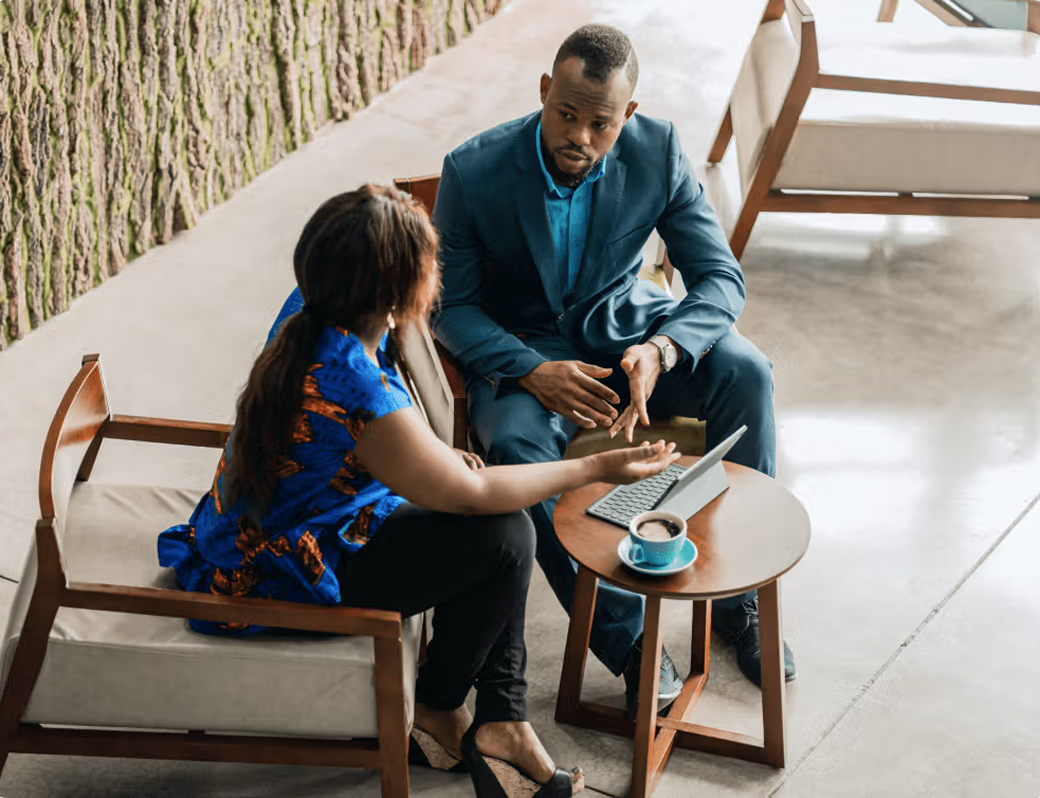 A man and a woman discuss at a table with a tablet and coffee.