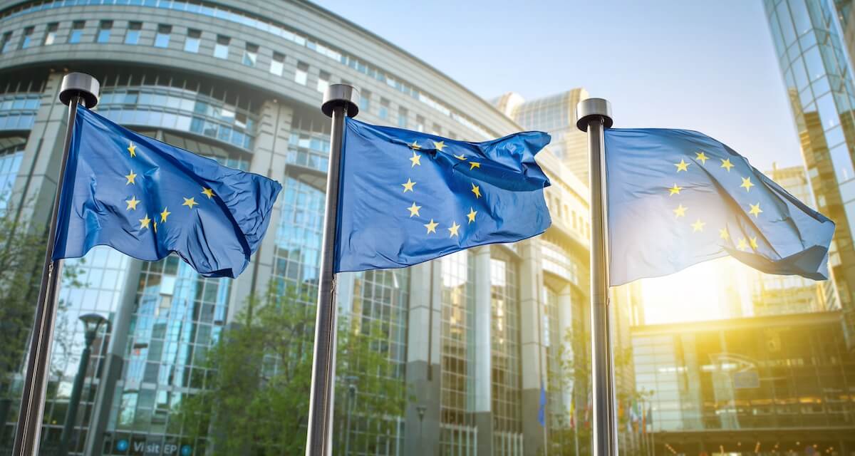 Three EU Flags flying in front of an urban city setting