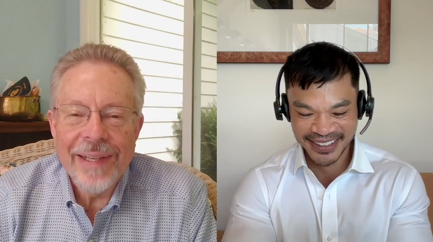 Two men are having a video call, both smiling; the man on the left is older with glasses and a light shirt, and the man on the right is younger with dark hair, a headset, and a white shirt.