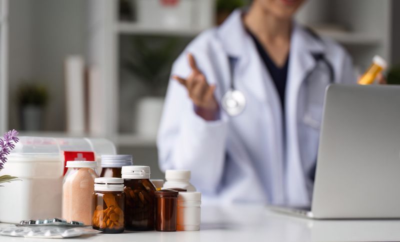Doctor consulting remotely with pill bottles and a first aid kit on the desk.