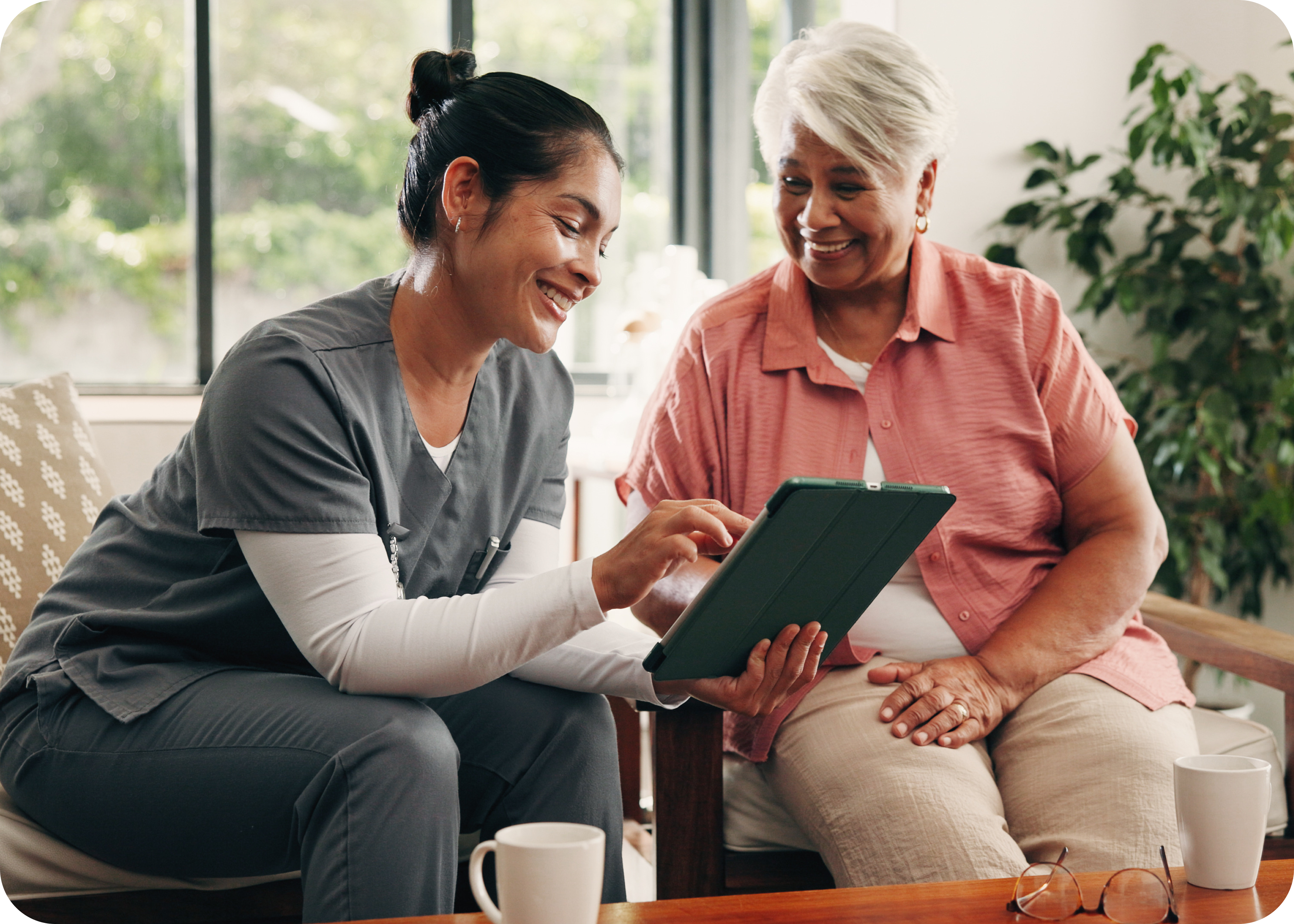 Smiling caregiver shows an older woman a tablet.