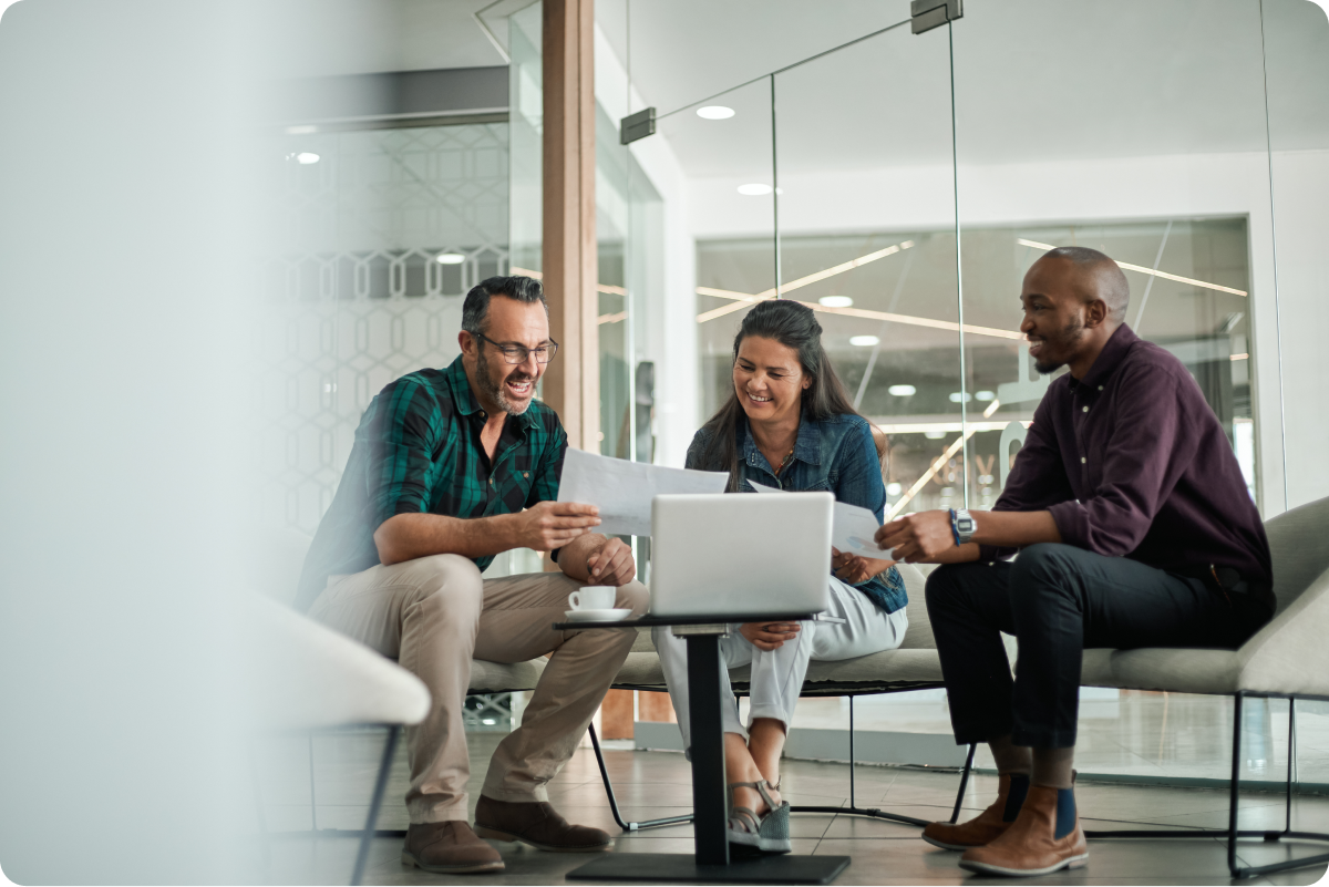 Three colleagues happily discussing data security for their customers in an office, reviewing documents on a computer
